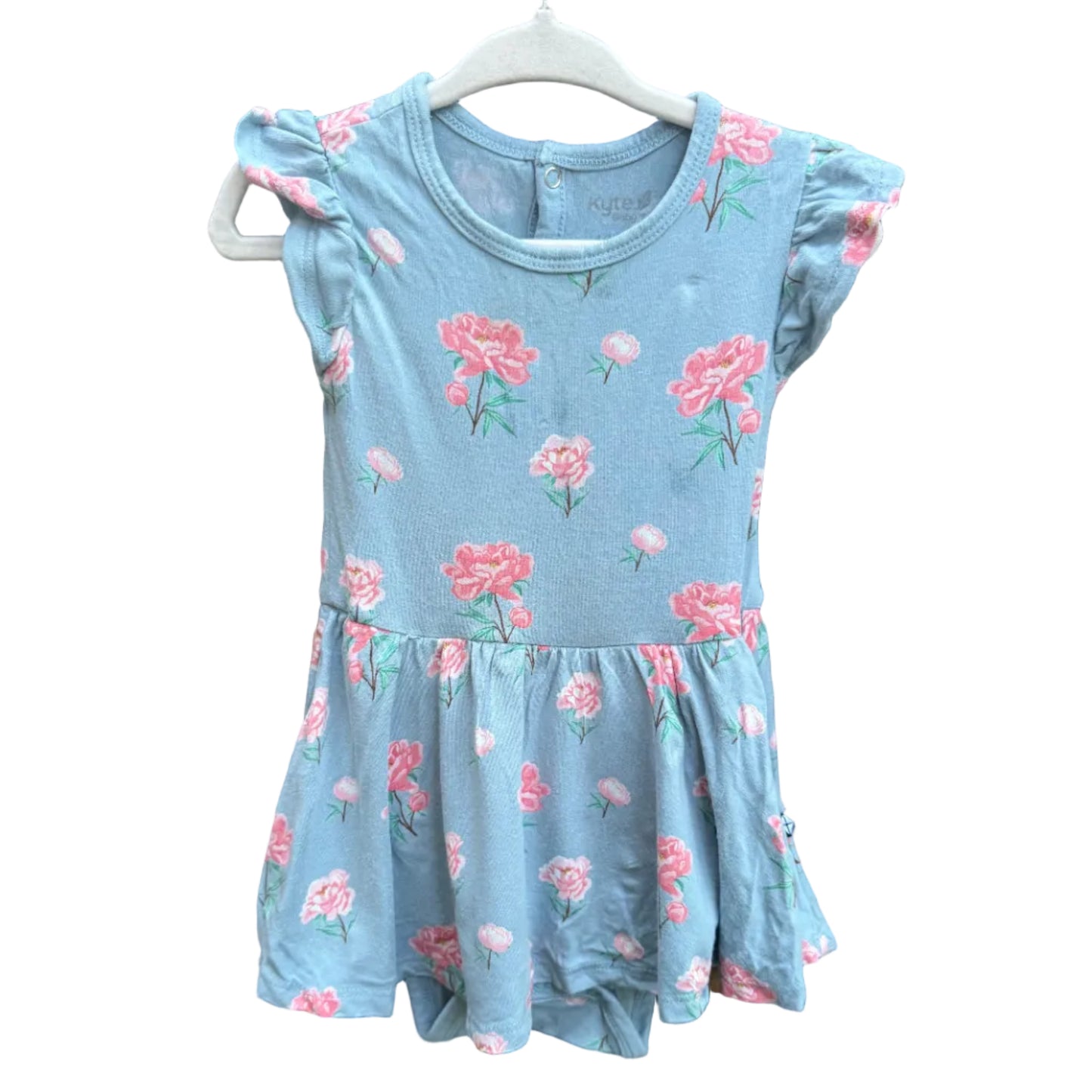 A light blue girls' dress with a pink and green floral print, featuring ruffled cap sleeves and a tiered skirt, hanging on a white plastic hanger against a brown brick wall.