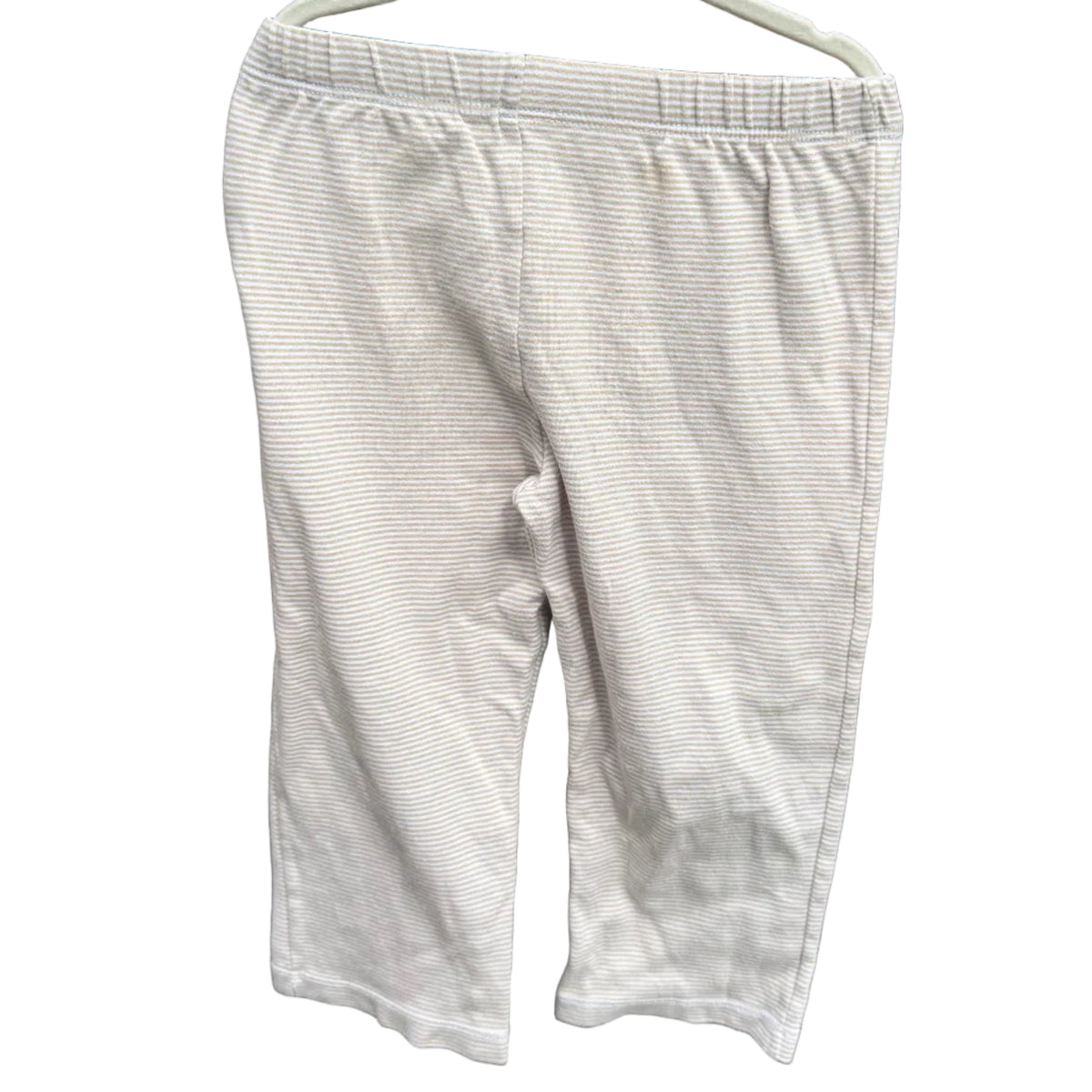A pair of light beige or off-white cropped pants hanging on a white plastic hanger against a red-brown brick wall with green foliage visible above.