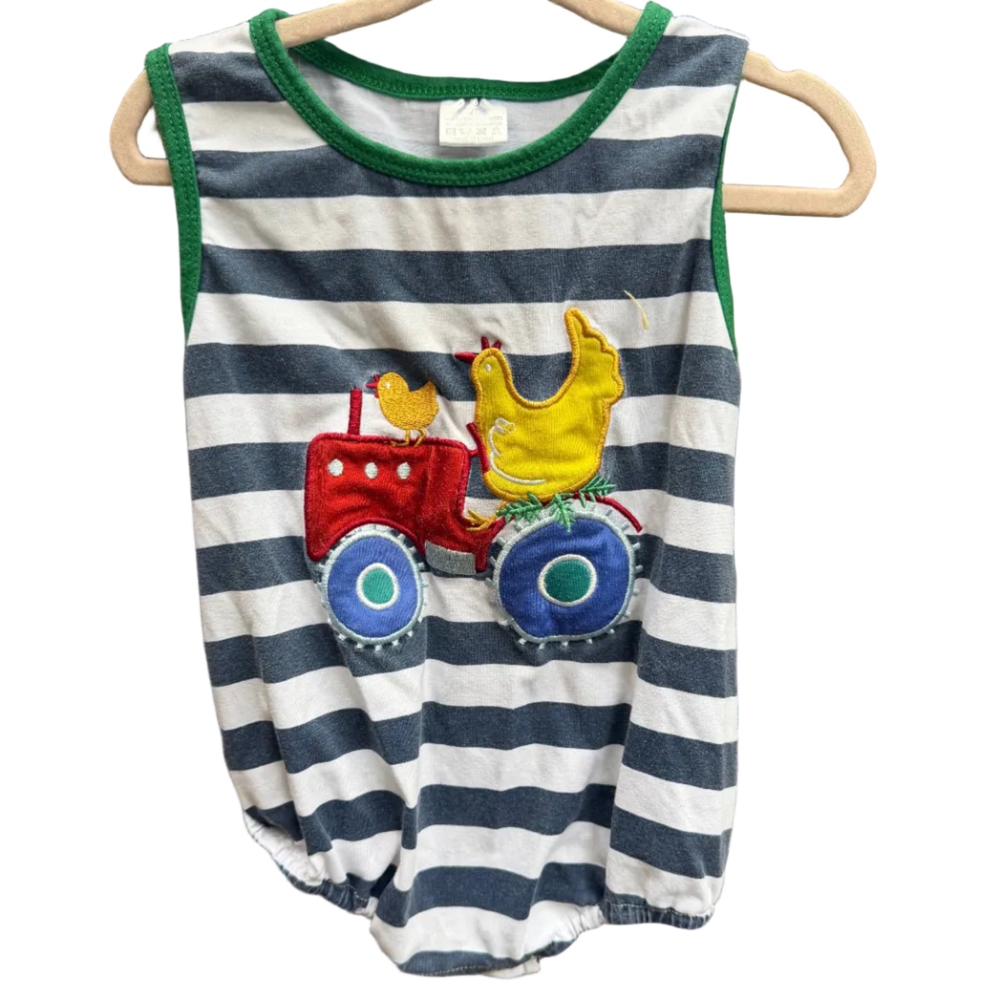 A sleeveless baby romper with navy and white horizontal stripes, green trim, and a colorful applique design of a red tractor and a yellow chicken, hanging on a wooden hanger against a brick wall.