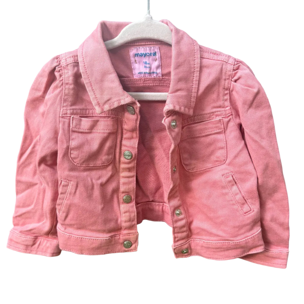 A pink denim jacket for kids, hanging on a white plastic hanger against a rustic brick wall background.