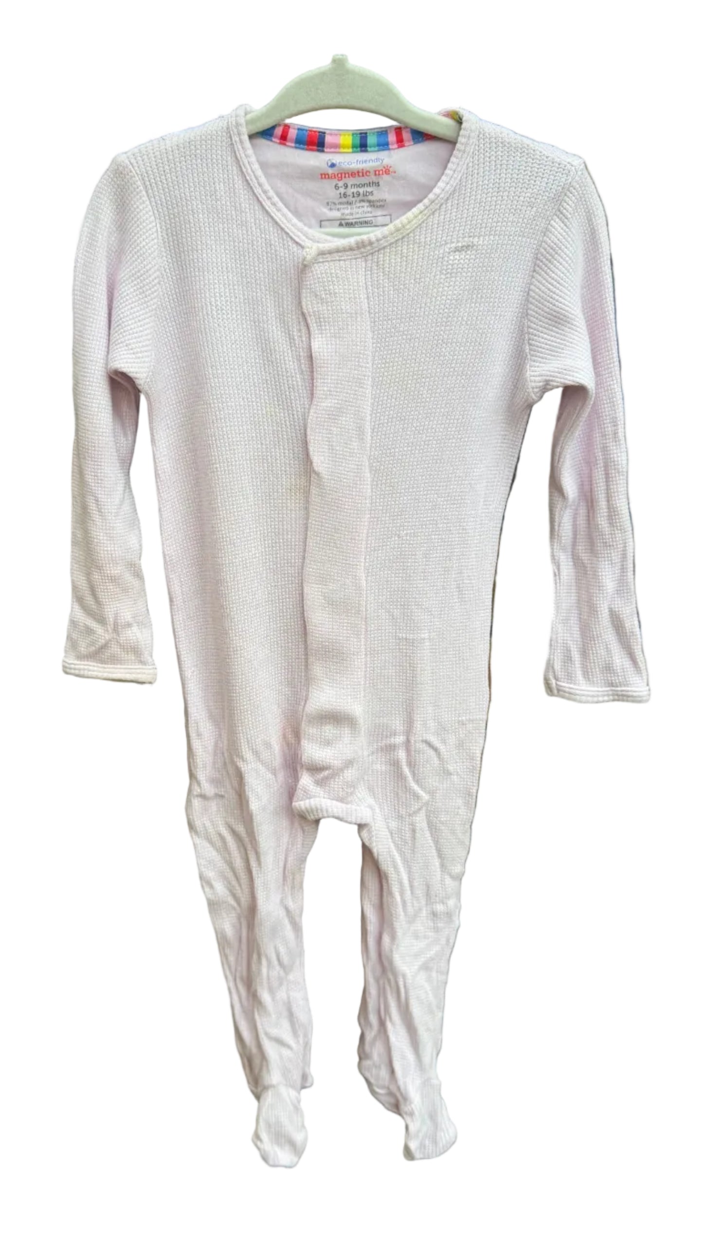 A light pink long-sleeve baby footed sleeper hanging on a hanger against a brick wall background.
