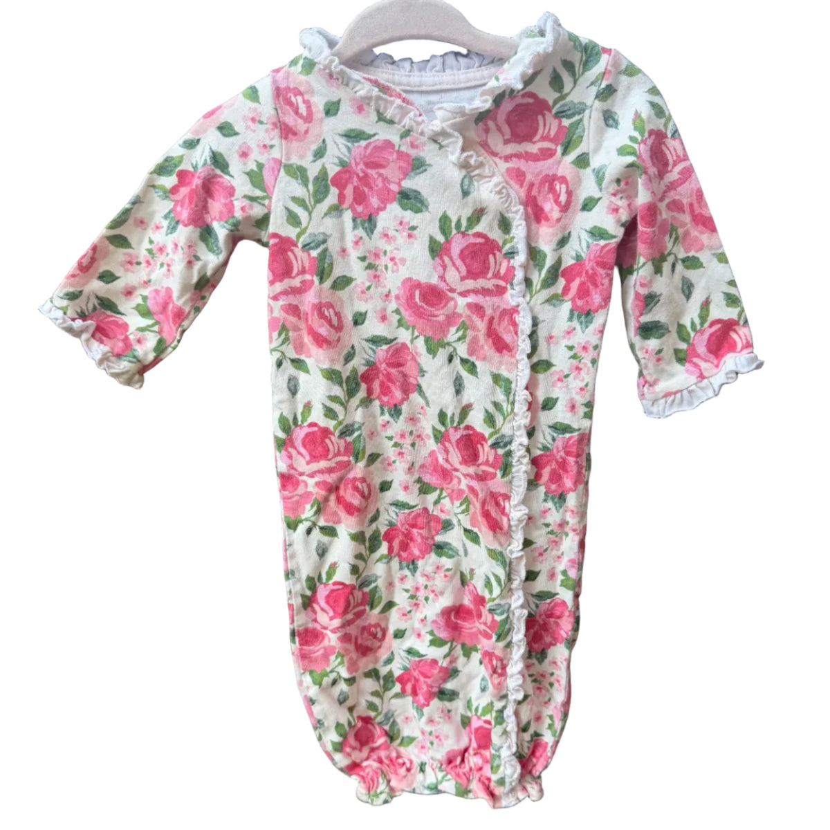 A baby long-sleeve bodysuit with a pink rose floral print on a cream background, hanging on a wooden hanger against a brick wall.