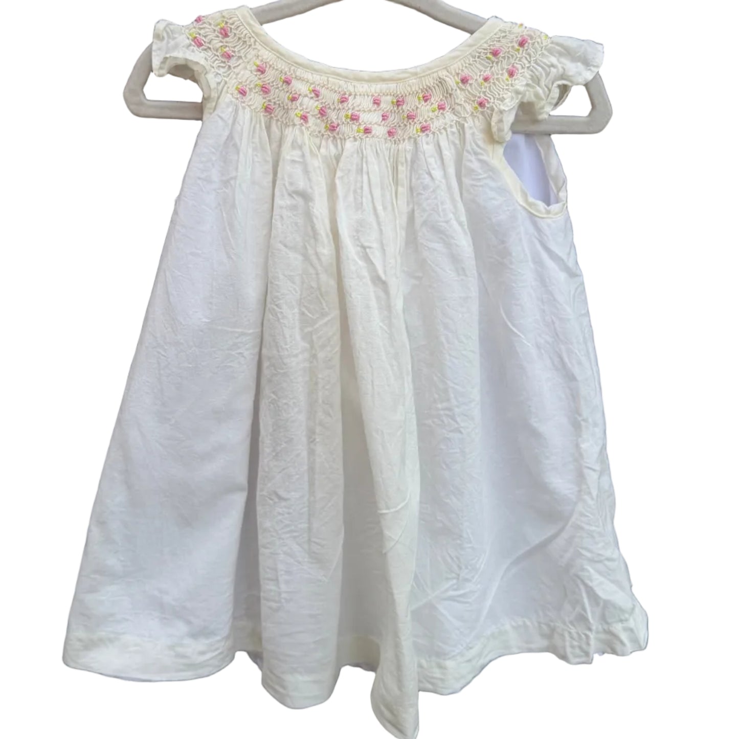A white baby girl's dress with pink and green floral embroidery around the neckline, hanging on a white plastic hanger against a brick wall background.