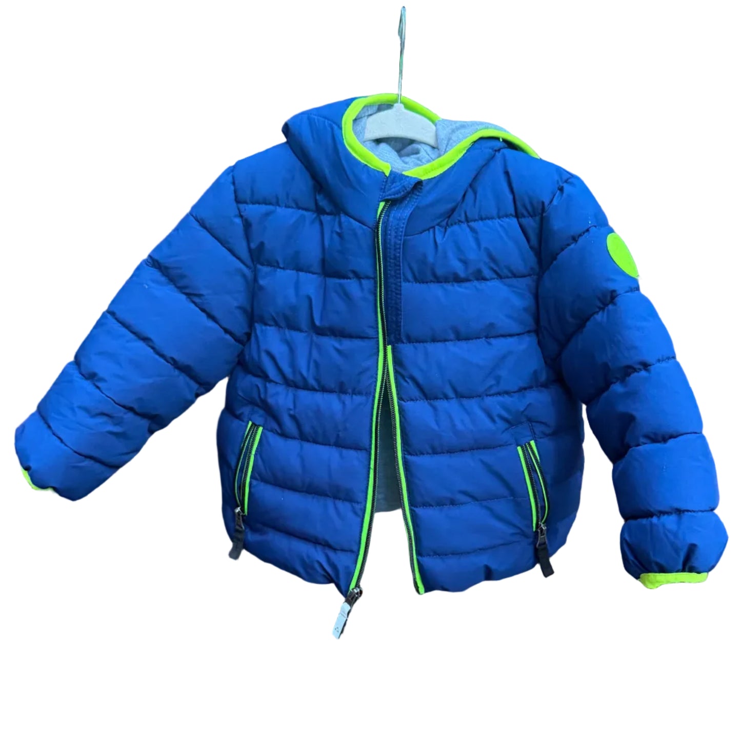A bright blue kids' puffer jacket with neon green trim hanging on a brick wall outdoors.