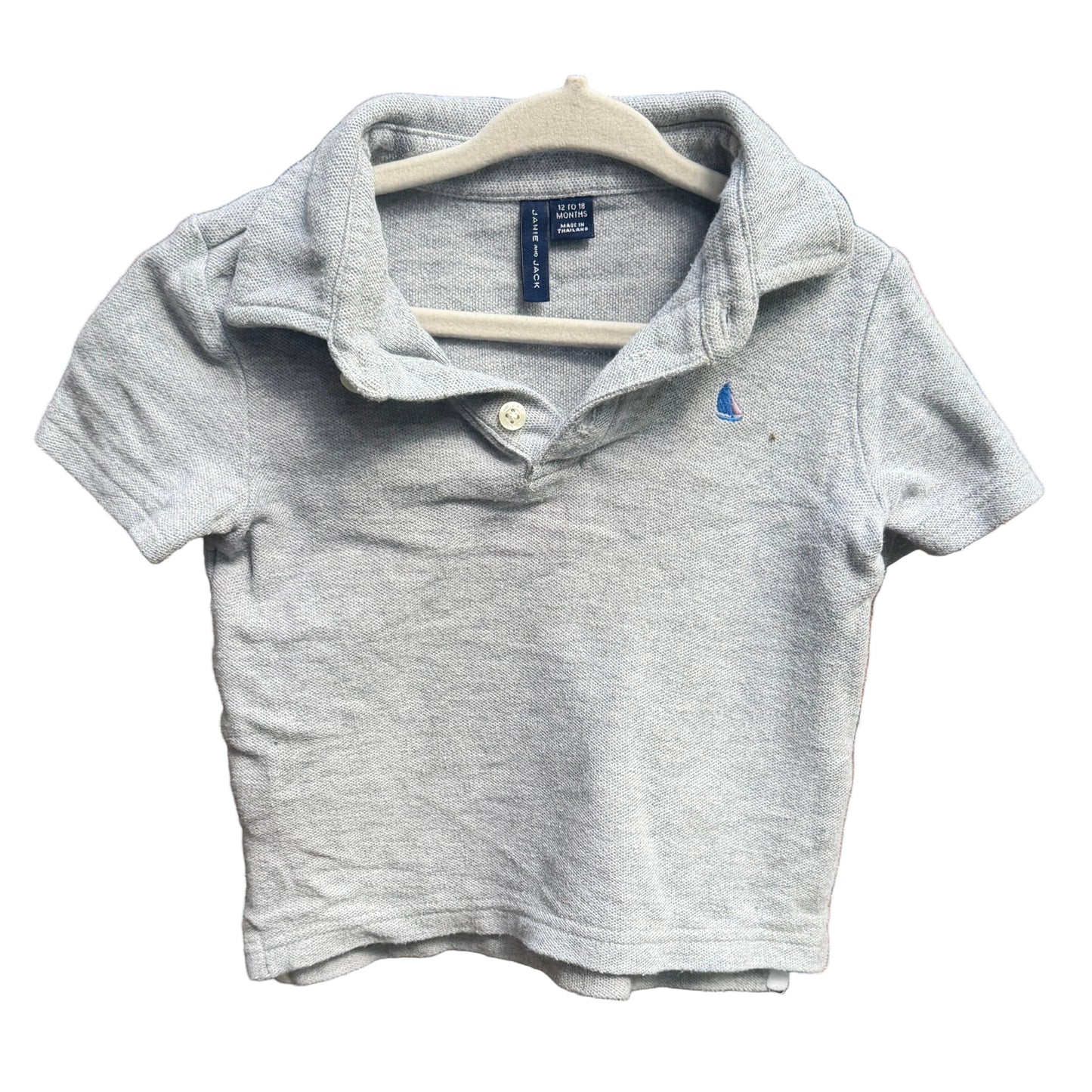 A light gray heather short-sleeve polo shirt for toddlers, featuring a small blue embroidered polo player logo on the left chest, hanging on a white plastic hanger against a red-brown brick wall.