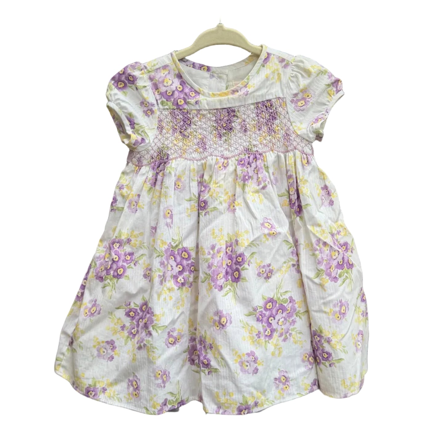 White dress with purple floral pattern on a hanger against a brick wall.