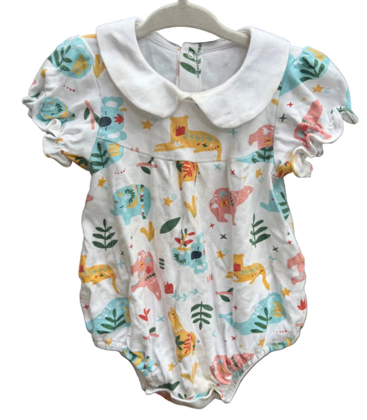 A baby romper with a white collar, featuring a colorful dinosaur and animal print on a white background, laid flat on a brown brick surface.
