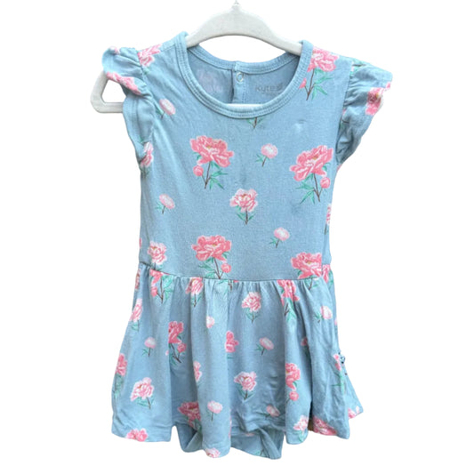 A light blue girls' dress with a pink and green floral print, featuring ruffled cap sleeves and a tiered skirt, hanging on a white plastic hanger against a brown brick wall.