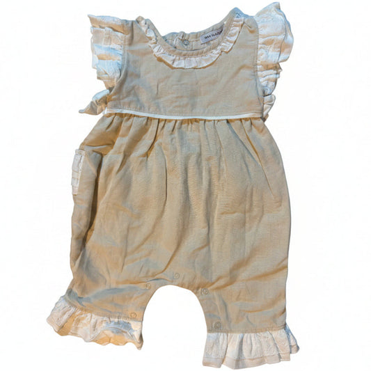 A baby romper in a light beige or cream-colored linen-like fabric, featuring ruffled trim at the neckline and leg hems, laid flat on a white blanket.