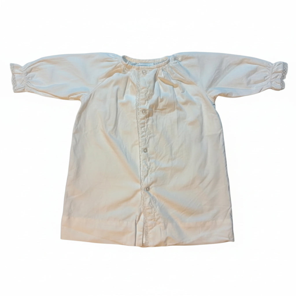 A cream-colored baby bodysuit or diaper cover laid flat on a white towel, showing a button-down front and ruffled trim details.