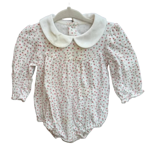 A baby girl's long-sleeve romper in white fabric with a tiny red and green floral print, featuring a large white Peter Pan collar, hanging on a white hanger against a brick wall.
