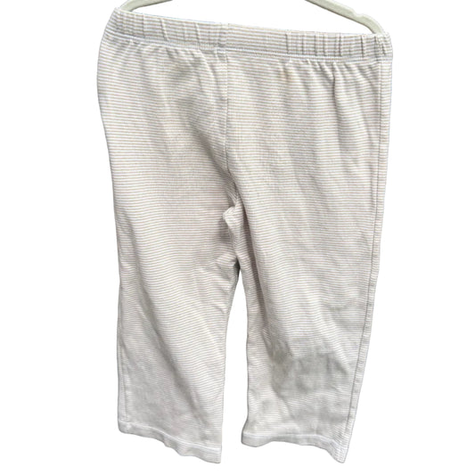 A pair of light beige or off-white cropped pants hanging on a white plastic hanger against a red-brown brick wall with green foliage visible above.