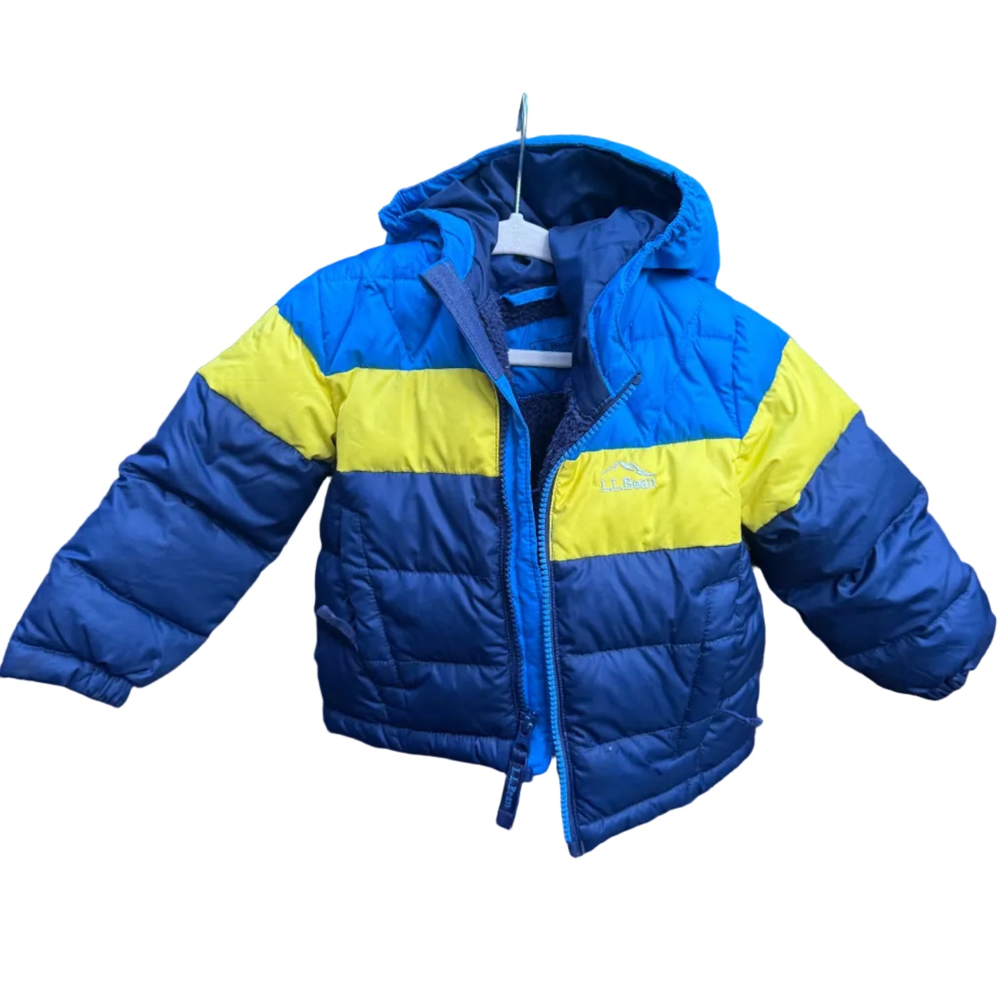 A blue and yellow hooded puffer jacket hanging on a brick wall outdoors, with trees and a stone visible in the background.