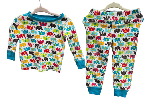 A children's two-piece pajama set hanging on wooden hangers against a brick wall outdoors. The set includes a long-sleeve top and matching pants with a colorful elephant print on a white background and solid blue cuffs and collar.