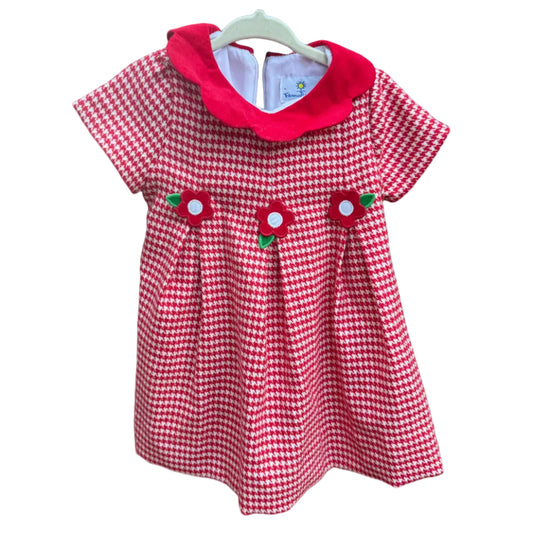 A short-sleeve baby dress with a red and white gingham pattern, a solid red Peter Pan collar, and three strawberry appliques on the front, hanging on a white plastic hanger against a brick wall.