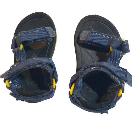 A pair of children's navy blue sandals with yellow accents, photographed from above on a light-colored surface.