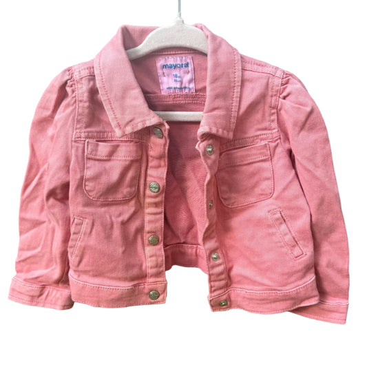 A pink denim jacket for kids, hanging on a white plastic hanger against a rustic brick wall background.