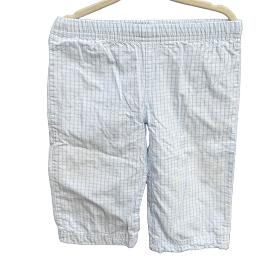 Light blue and white checkered shorts hanging on a beige hanger against a red-brown brick wall with green foliage in the background.