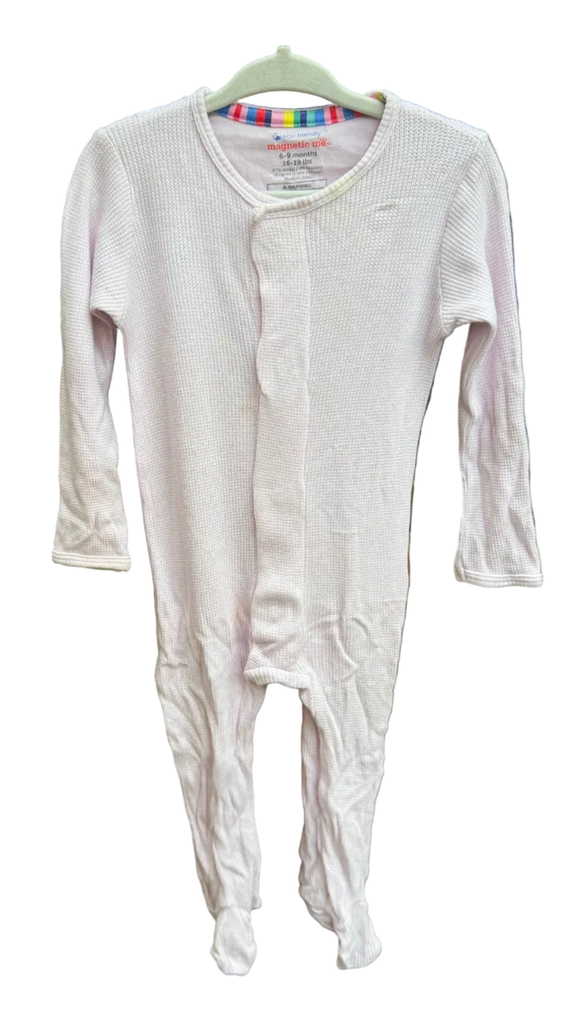 A light pink long-sleeve baby footed sleeper hanging on a hanger against a brick wall background.