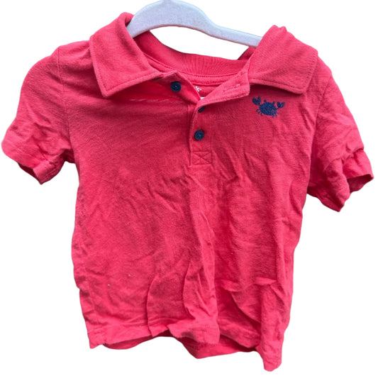 A pink short-sleeve polo shirt for a toddler, hanging on a white plastic hanger against a brick wall background.