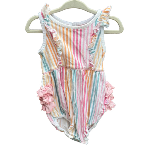 A baby girl's sleeveless romper with pastel vertical stripes in pink, orange, yellow, blue, and white, featuring ruffle details on the shoulders and hips, hanging on a white plastic hanger against a brown brick wall.