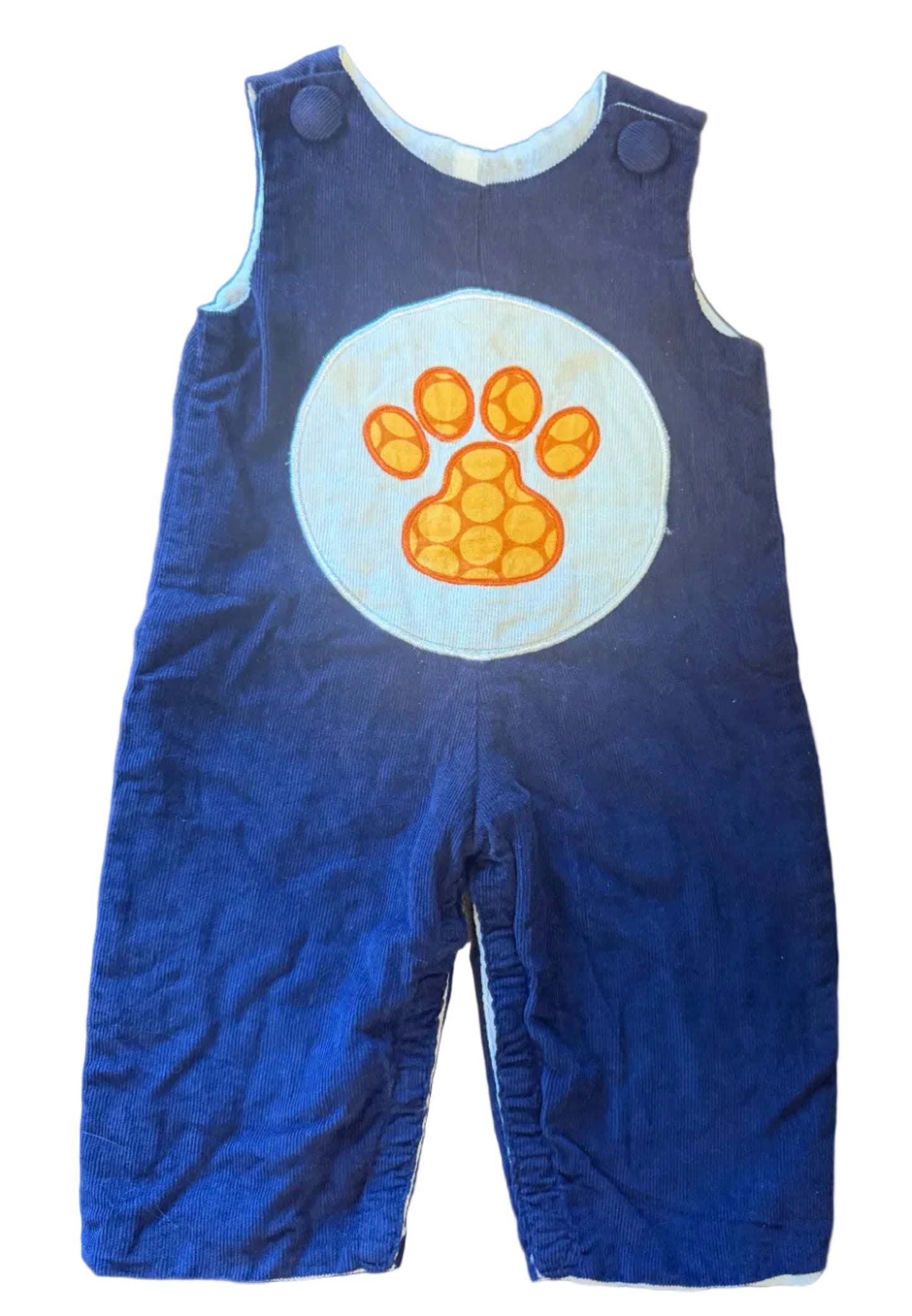 A baby blue corduroy romper with a large white circular patch on the chest featuring an orange paw print, laid flat on a wooden surface.