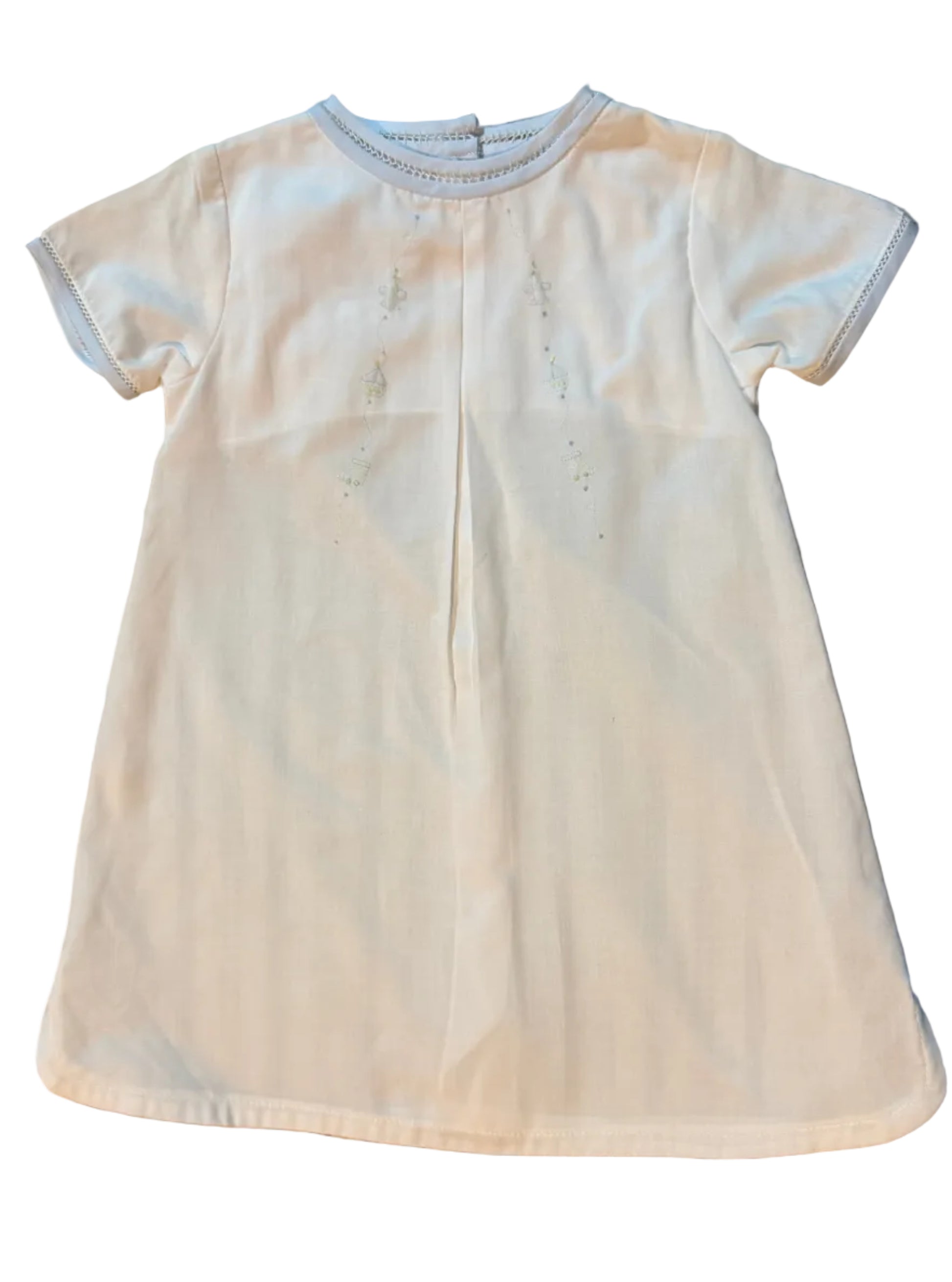 A white short-sleeve baby t-shirt with a center back opening and subtle embroidered details, laid flat on a striped gray and white surface.