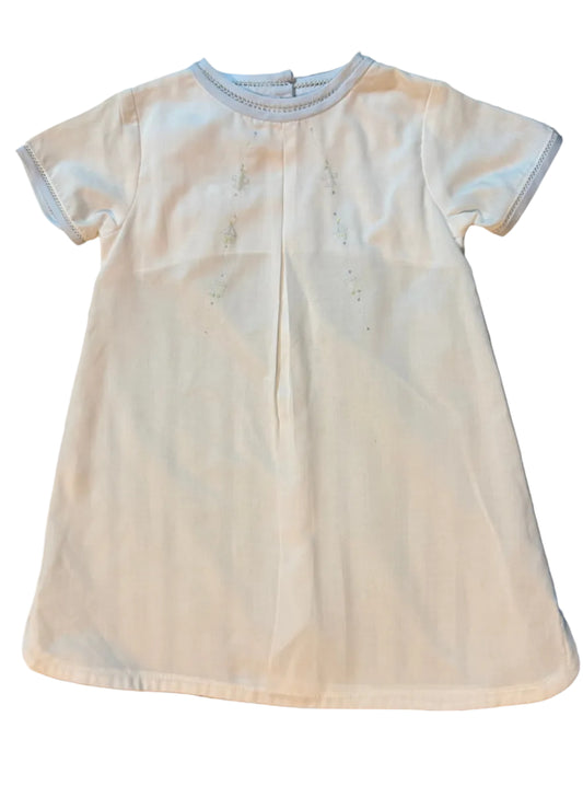 A white short-sleeve baby t-shirt with a center back opening and subtle embroidered details, laid flat on a striped gray and white surface.