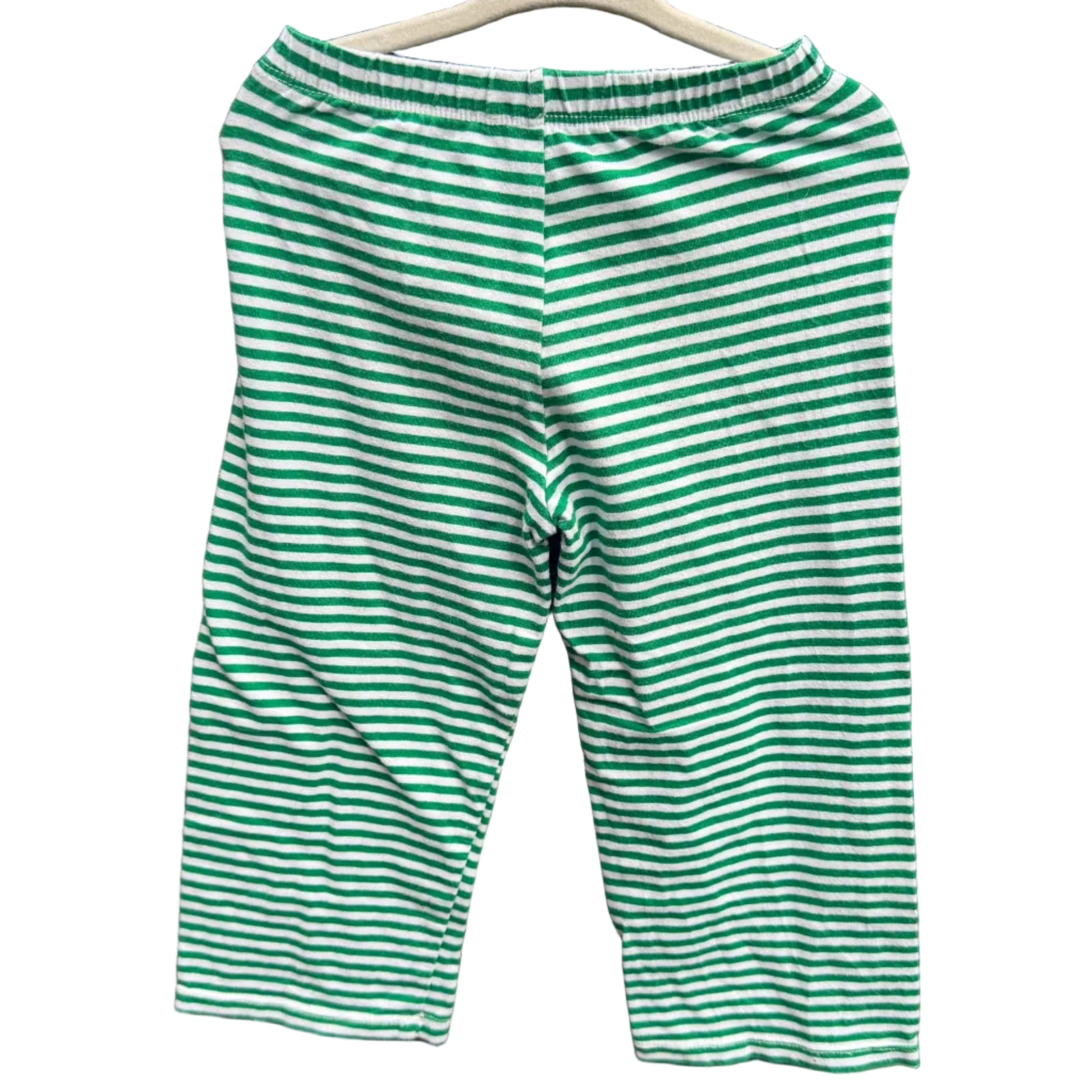 Green and white striped knit capri pants hanging on a wooden hanger against a red-brown brick wall.