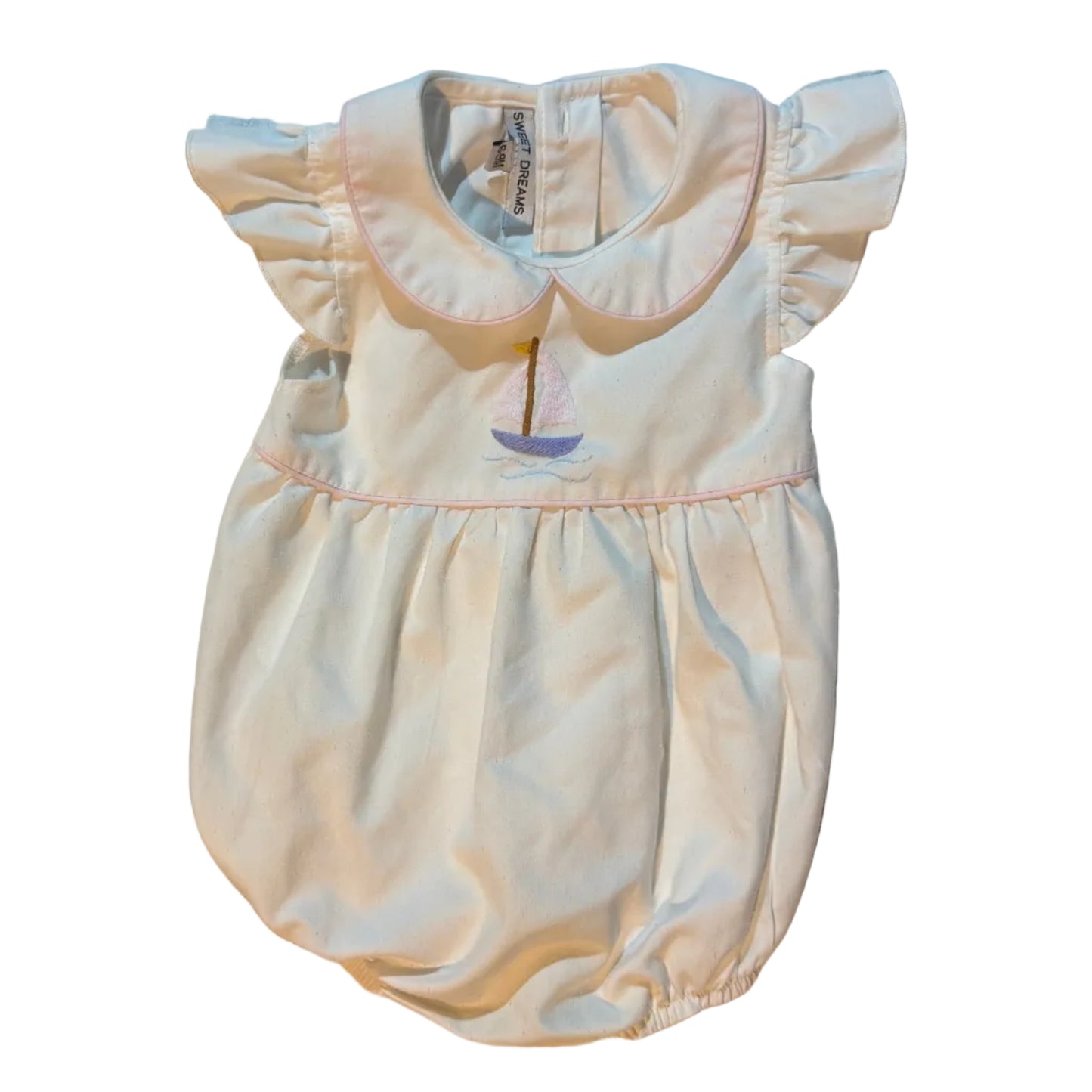 A baby girl's cream-colored dress with a Peter Pan collar and flutter sleeves, laid flat on a white towel. The dress features a small embroidered sailboat motif at the center chest.