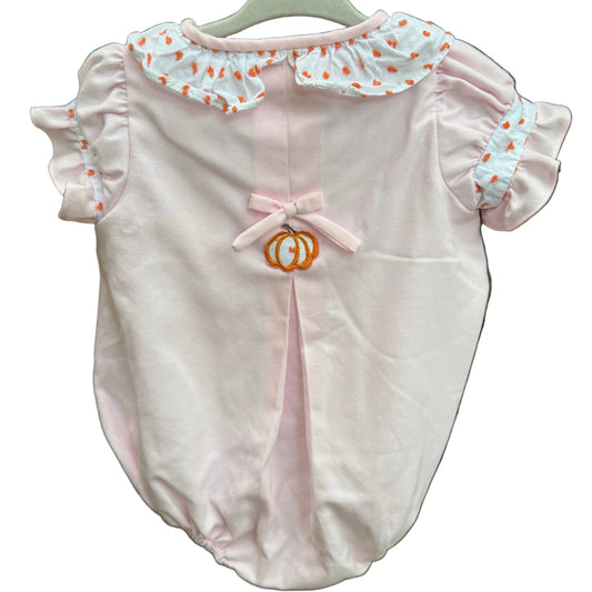 A light pink baby romper with ruffled collar and sleeves, featuring a small orange embroidered monogram on the chest, hanging on a white hanger against a brick wall.