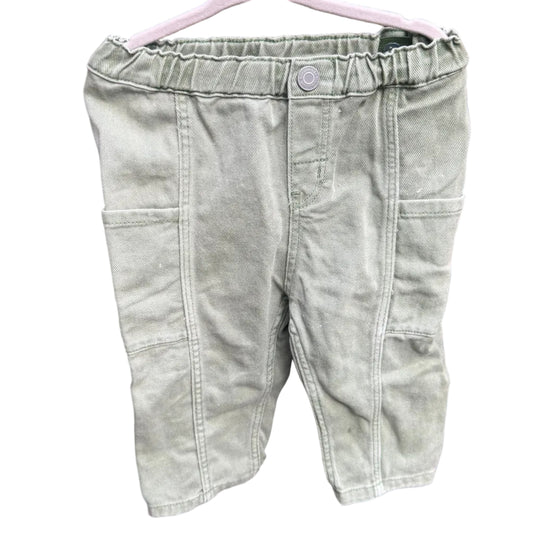A pair of light sage green denim shorts hanging on a white plastic hanger against a red-brown brick wall.