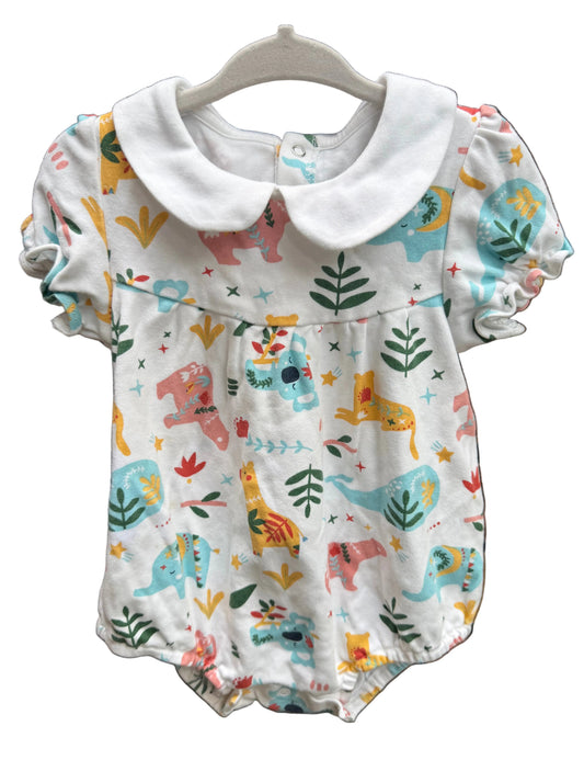 A baby romper with a white Peter Pan collar, featuring a colorful dinosaur and plant print on a white background, hanging on a white plastic hanger against a brown brick wall.