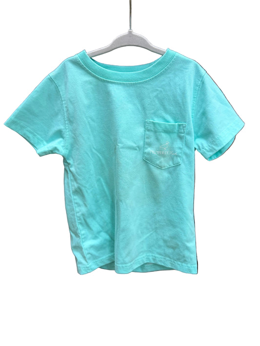 A mint green short-sleeve pocket t-shirt hanging on a white plastic hanger against a red-brown brick wall.