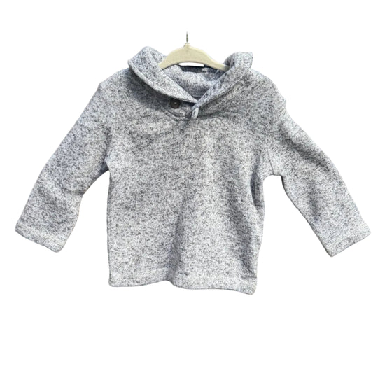 A light gray marled knit hooded sweater with three-quarter sleeves hangs on a wooden hanger against a brick wall with green trees in the background.