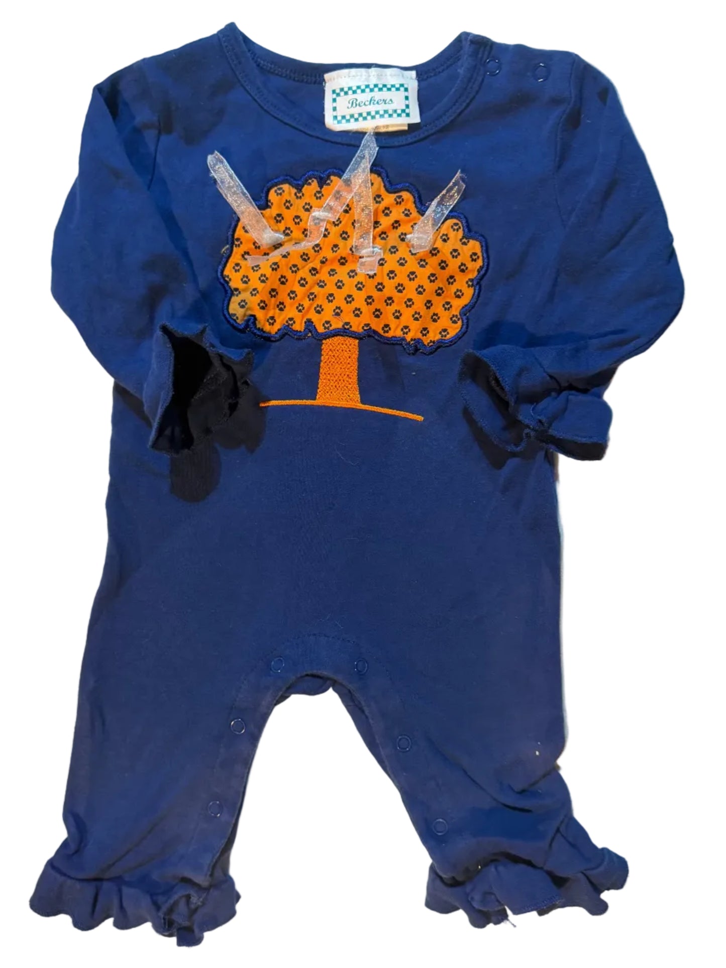 A navy blue baby bodysuit with ruffled sleeves and legs, featuring a novelty poop graphic on the front in orange and black with clear plastic pull tabs, laid flat on a white towel.
