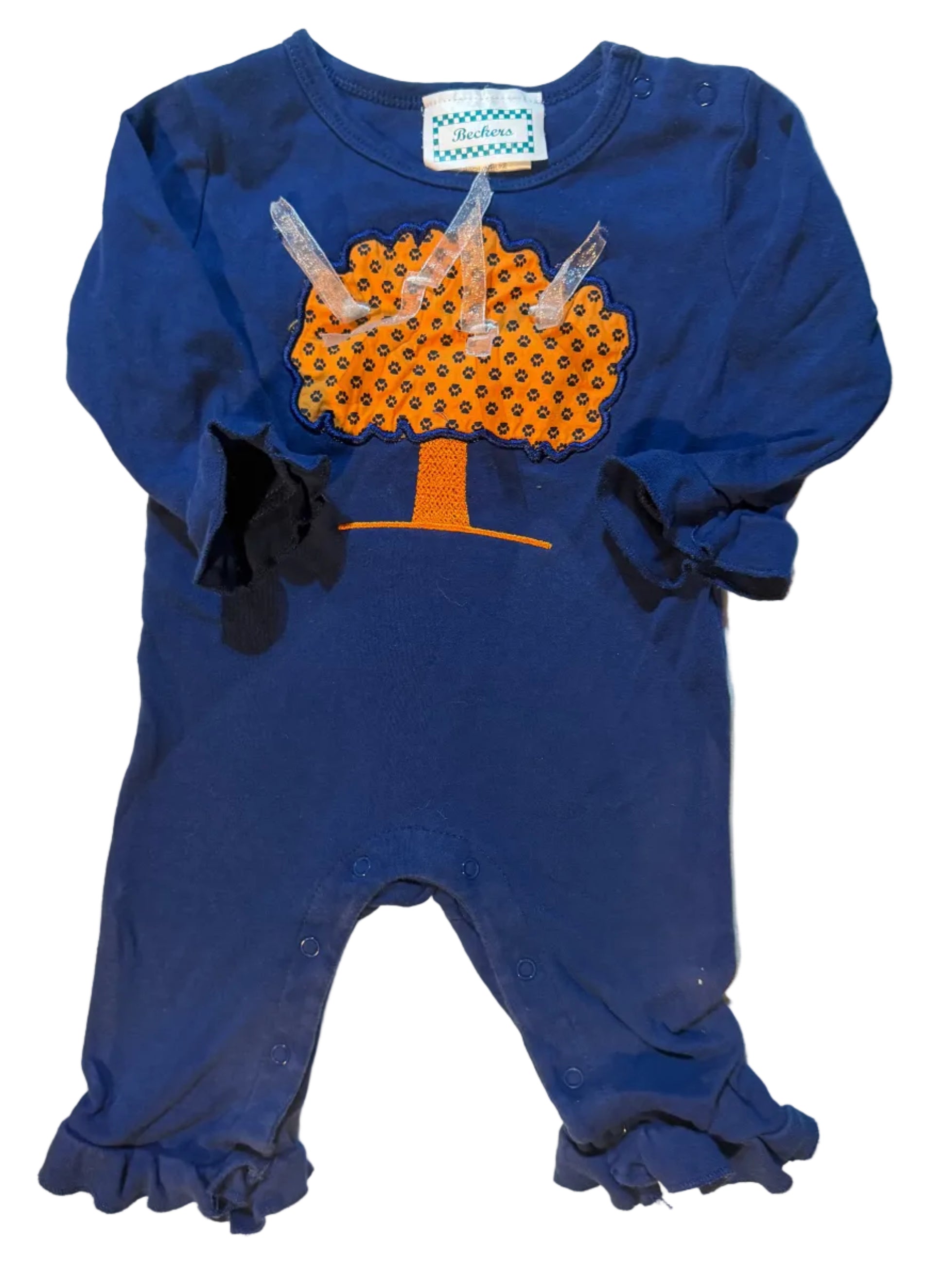 A navy blue baby bodysuit with ruffled sleeves and legs, featuring a novelty poop graphic on the front in orange and black with clear plastic pull tabs, laid flat on a white towel.