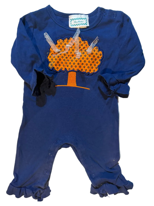 A navy blue baby bodysuit with ruffled sleeves and legs, featuring a novelty poop graphic on the front in orange and black with clear plastic pull tabs, laid flat on a white towel.
