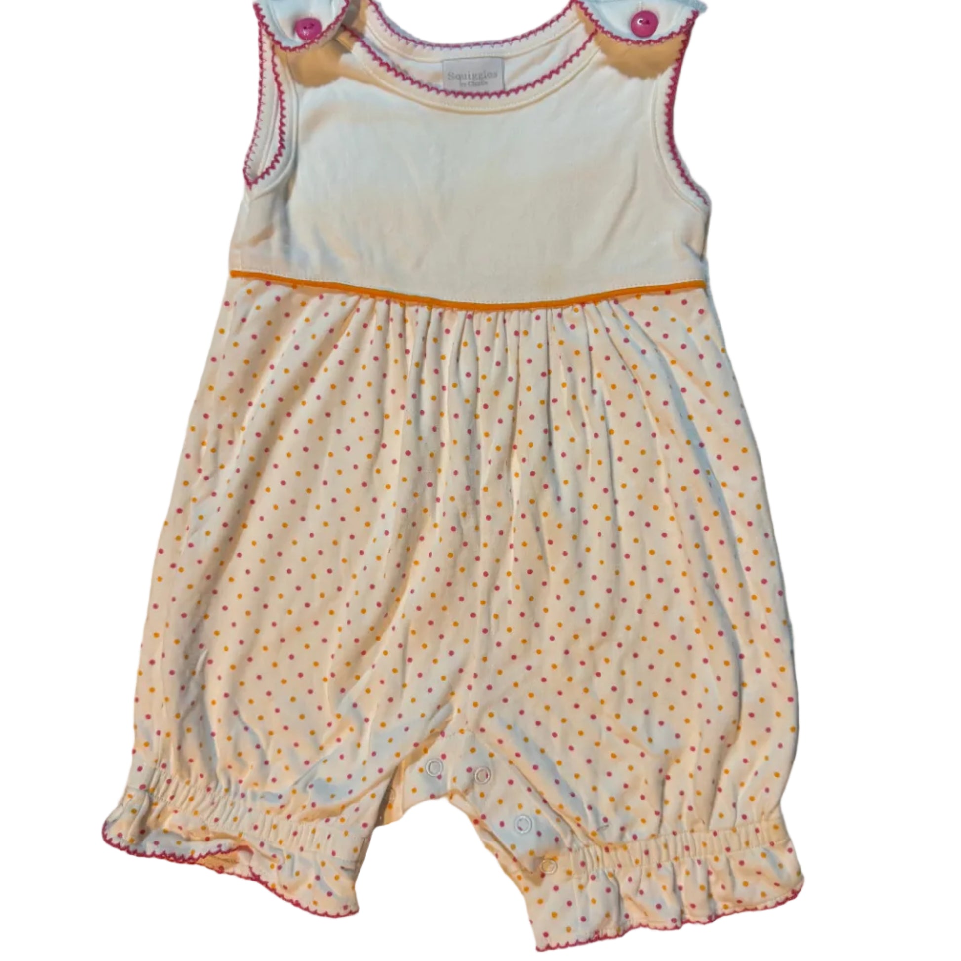 A baby bodysuit or romper laid flat on a white towel. The bodysuit has a cream-colored fabric with small orange and pink polka dots, gathered elastic cuffs, and a solid cream belly panel with embroidered details.
