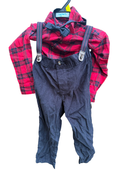 A toddler boy's clothing set consisting of a red and black plaid long-sleeve shirt, a black bow tie, and dark navy blue corduroy suspenders, hanging on a brick wall.