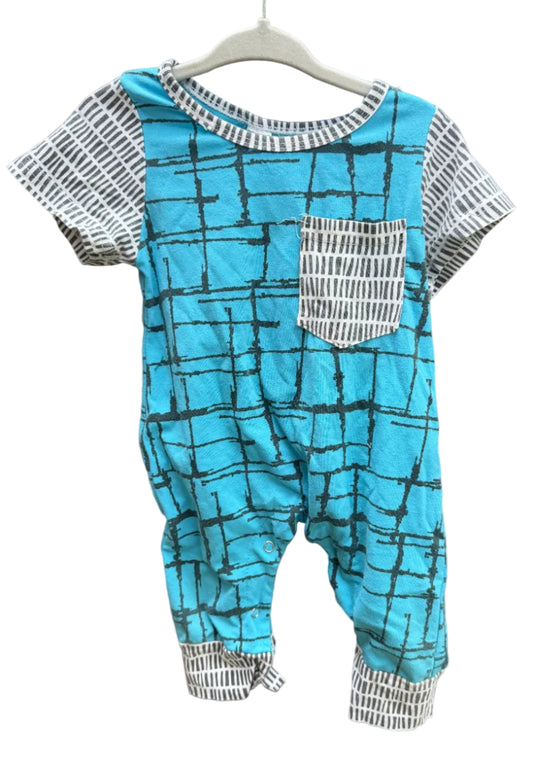 A baby short-sleeve romper with a bright turquoise blue body featuring a black grid pattern, paired with white and black patterned sleeves, pocket, and cuffs, hanging on a white hanger against a red-brown brick wall.