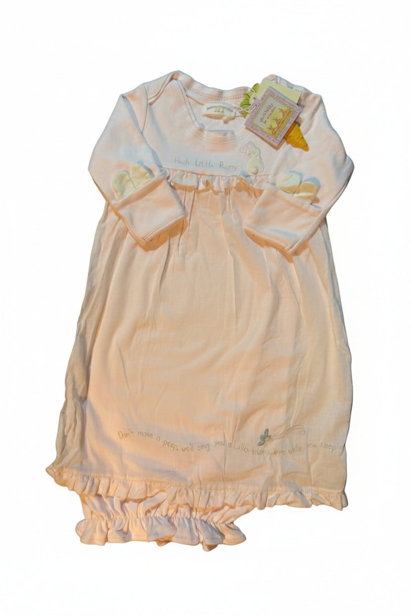 A pale pink baby romper with ruffled trim and a ruffled waistband, laid flat on a white towel. The garment has a small yellow graphic on the lower left leg and a hangtag attached.