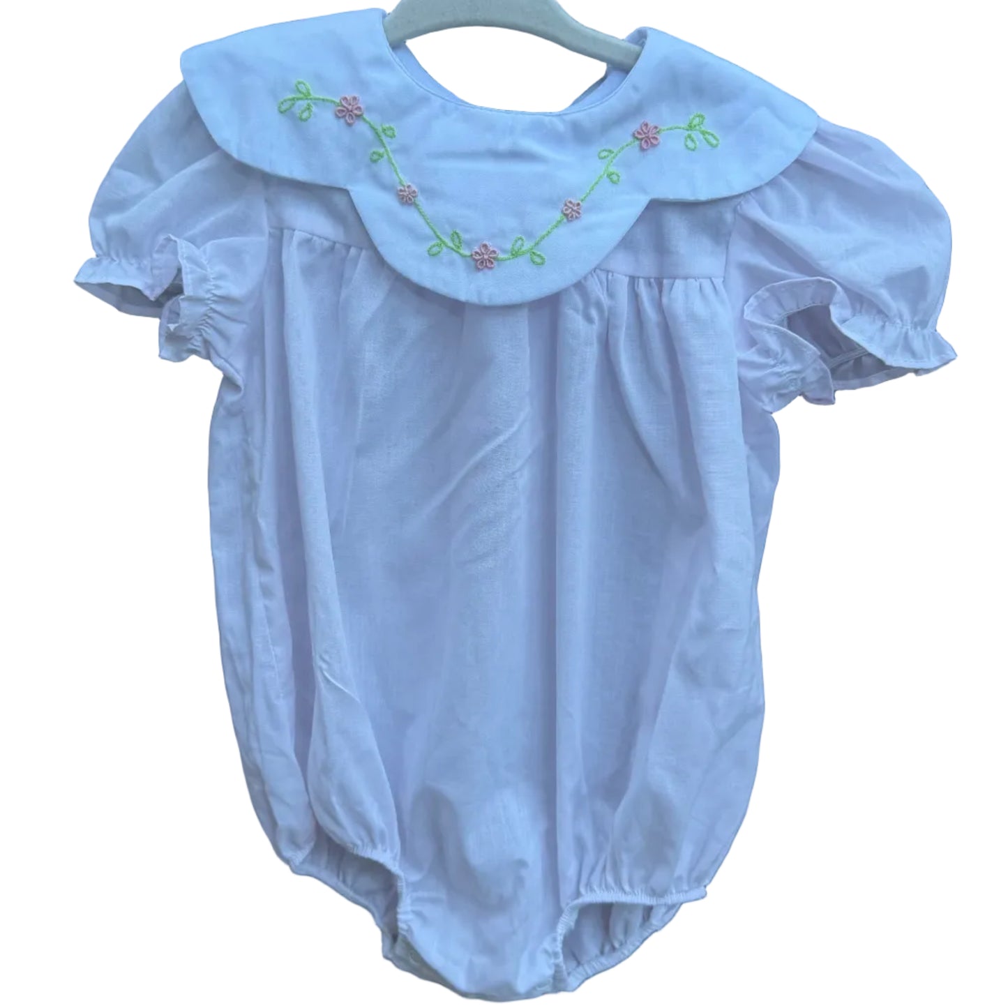 A pink baby bubble romper with a large embroidered Peter Pan collar, hanging on a white plastic hanger against a brick wall background.