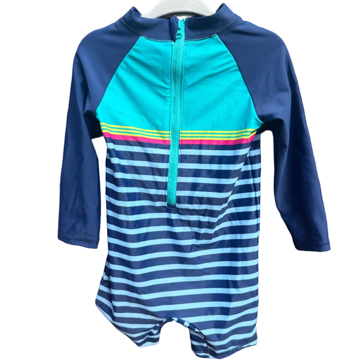 A children's long-sleeve one-piece swimsuit or rash guard hanging on a white hanger against a brick wall. The top portion is bright turquoise with a half-zip front, navy sleeves, and thin multicolor horizontal stripes across the chest.