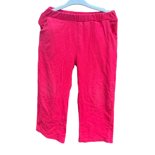 Bright pink cropped pants hanging on a white hanger against a brown brick wall background.