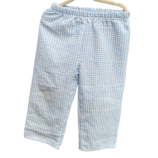 Light blue and white checkered cropped pants hanging on a white plastic hanger against a red-brown brick wall.