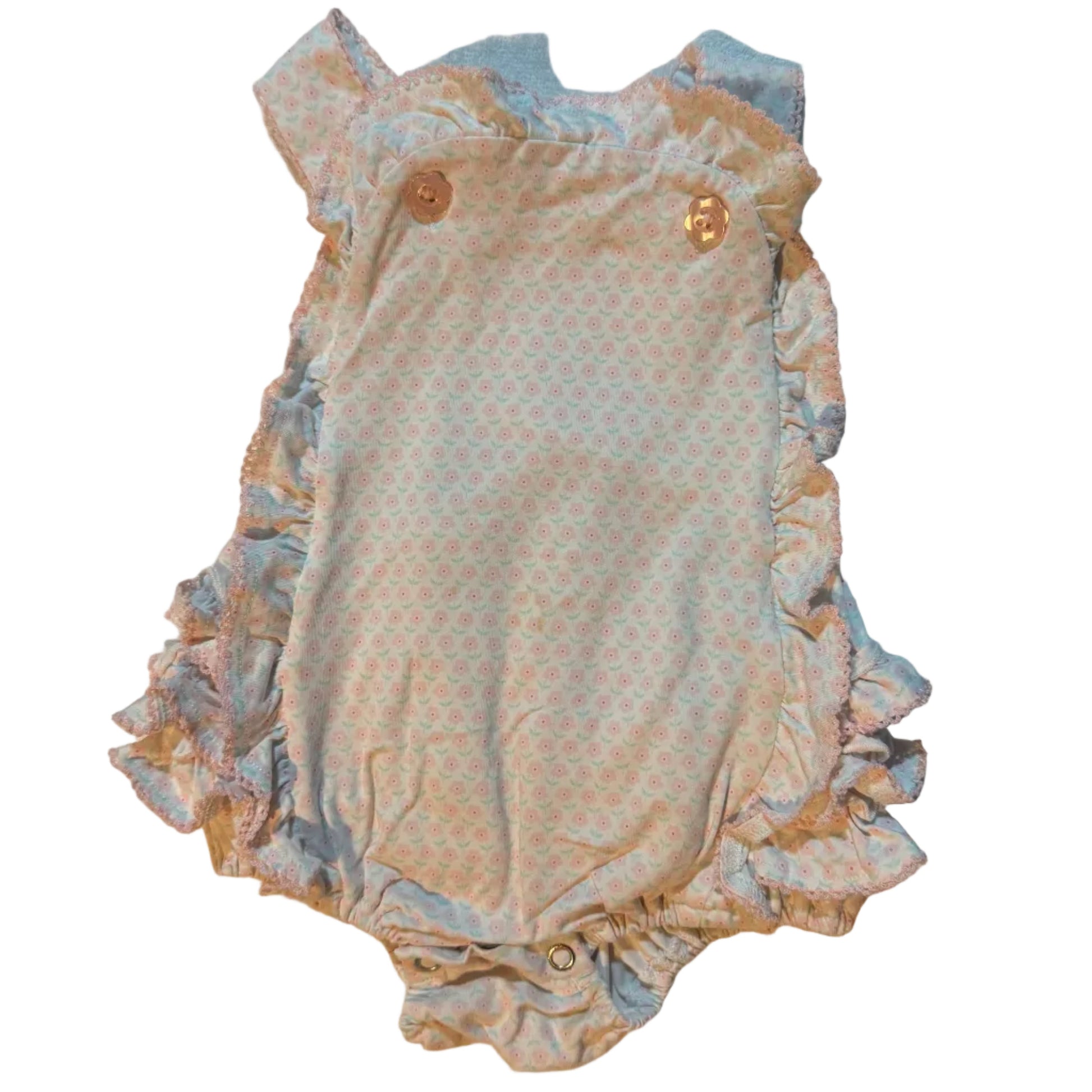 A vintage-style baby bodysuit or romper with ruffled trim, laid flat on a beige towel. The bodysuit features a light peach and blue patterned center with a solid peach ruffled border and three gold snap buttons.