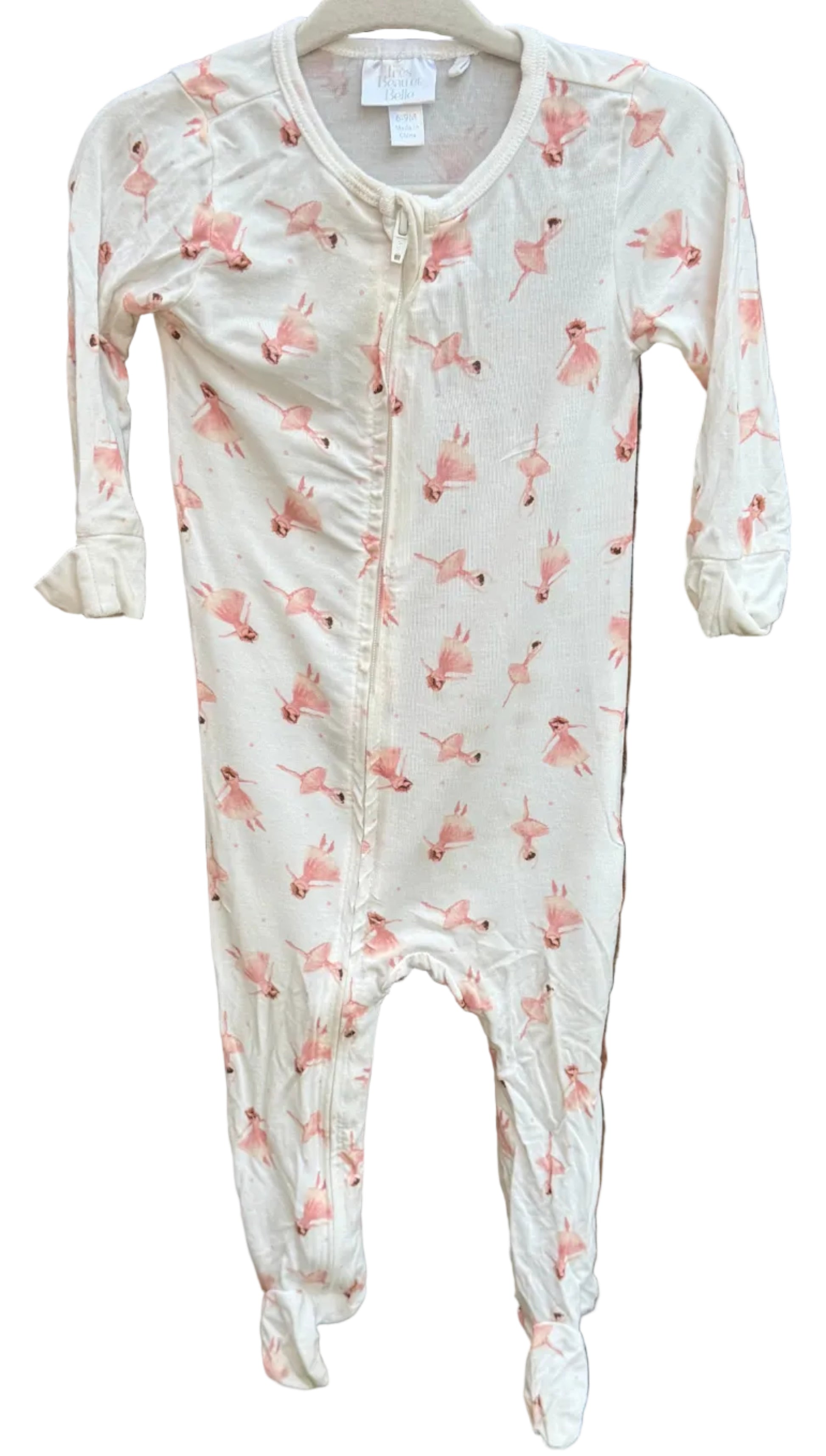 A baby footed sleeper in an off-white/cream color with a pink flamingo print, hanging on a white plastic hanger against a brick wall.