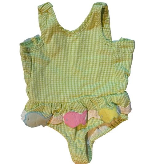 A small green and white gingham one-piece swimsuit with ruffled trim and three pastel appliqués in pink, yellow, and blue, laid flat on a white towel.