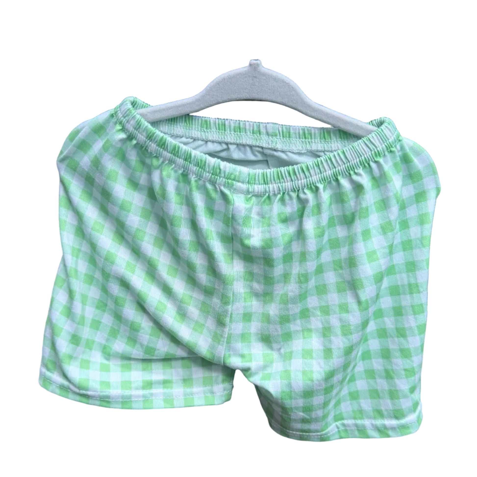 Green and white gingham check boxer shorts hanging on a white plastic hanger against a red-brown brick wall.